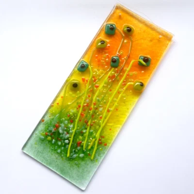 At a slight angle detail of textured orange and green glass frit on a handcrafted floral fused glass window hanging.