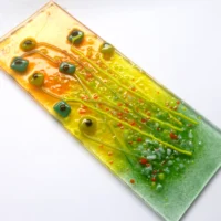 Close-up detail of textured orange and green fused glass floral suncatcher with frit..