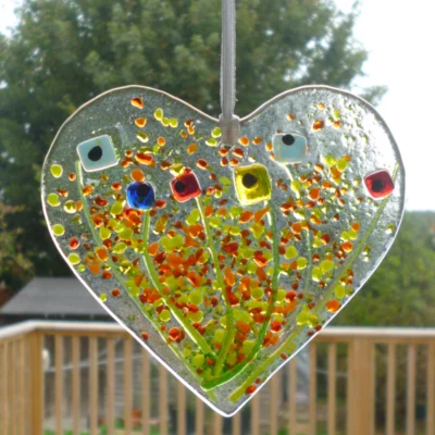 Fused glass heart suncatcher hanging in a window from a white ribbon.