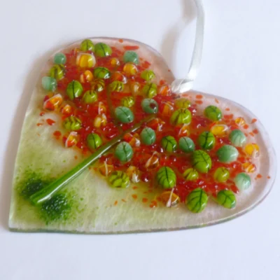 Fused glass heart suncatcher laying at an angle showing detail of autumn tree in green and red.