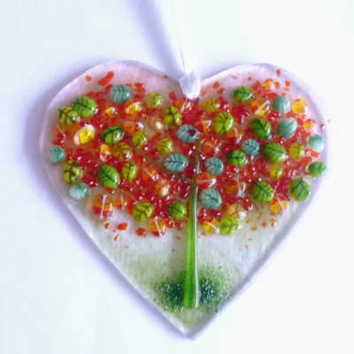 Fused glass heart suncatcher with autumn tree on top, with green and red leaves with green trunk. Hole at the top with white ribbon threaded through to hang from.