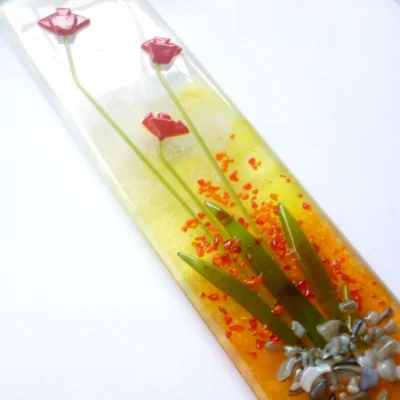 Close-up detail of raised tactile red glass flowers and leaves on a multi-coloured kiln-fused glass window panel.