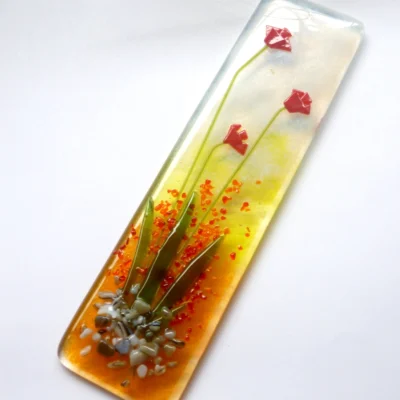 Fused glass red flower suncatcher laying at a slight angle on a neutral background.