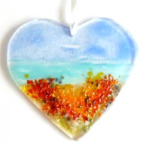 Fused glass suncatcher with blue and turquoise background, with yellow and orange flowers at the bottom. Hangs from a white ribbon.