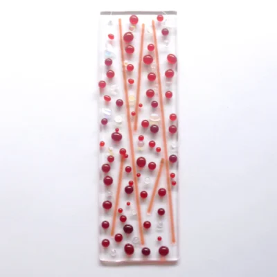 A bubbly red fused glass suncatcher with red and dichroic glass beads and stringers fused onto an oblong shaped piece of clear glass.