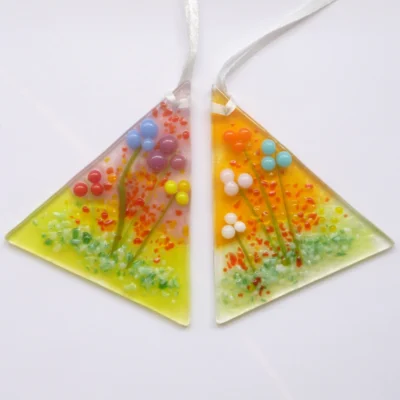 Set of two handmade glass flower suncatchers in a triangle shape with beads of colourful glass to create flowers in red, blue, turquoise, plum, orange, pink, yellow and white. Hole drill at the top point and has a white ribbon threaded through. Green and red creates more decoration. Very tactile and colourful