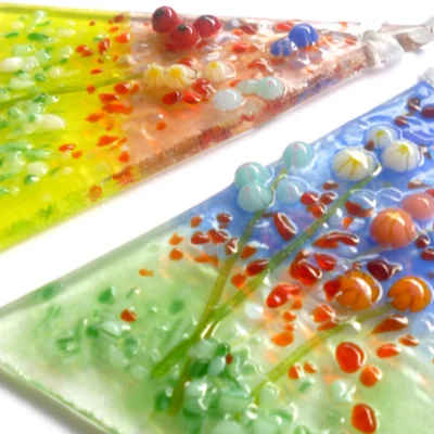 Close up of two small triangle shaped fused glass flower suncatchers, showing detail and colour of glass.