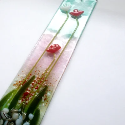 Long slim fused glass red flower suncatcher laying at an angle showing detail of glass.