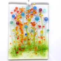 Handmade rectangle multicoloured glass flower suncatcher in colours of blue, yellow, orange, green, yellow and red. Quirky flowers have been created using glass beads and stringers for stems. Hangs from a white ribbon.
