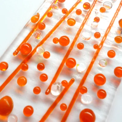 Close up of orange fused glass suncatcher with orange beads and stringers and dichroic beads. This is a very tactile design.