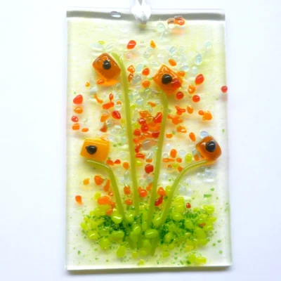 Rectangle orange fused glass flower suncatcher hanging from a white ribbon. Quirky square flower with vibrant red, orange and green frit for decoration.