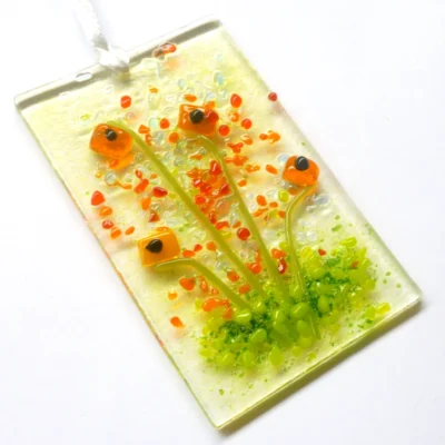 Handmade orange glass flower suncatcher laying an angle on a white background. Hangs from a white ribbon.