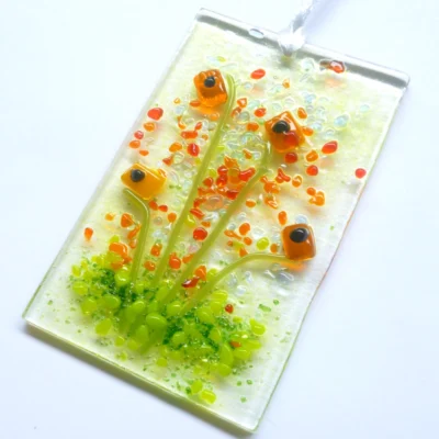 Rectangle handmade orange glass flower suncatcher, with red, orange and green frit as decoration. Hangs from a white ribbon.