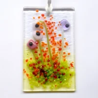 Rectangle Pink and lilac glass flower suncatcher hanging from a white ribbon. Red, orange and green frit for decoration.