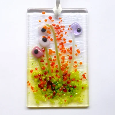 Rectangle Pink and lilac glass flower suncatcher hanging from a white ribbon. Red, orange and green frit for decoration.