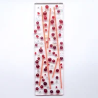 A bubbly red fused glass suncatcher with red and dichroic glass beads and stringers fused onto an oblong shaped piece of clear glass.
