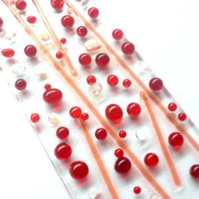 Close up of red fused glass suncatcher with red beads and stringers with a touch of dichroic beads. Tactile design.