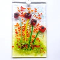 Rectangle red glass flower suncatcher with colourful frit decoration. Square red quirky flowers with green stems. Hangs from white ribbon.