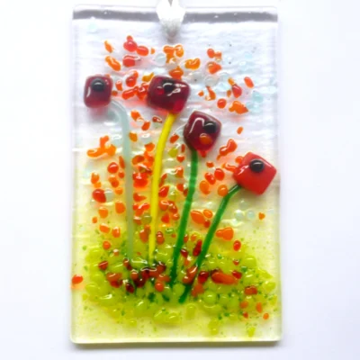 Rectangle red glass flower suncatcher with colourful frit decoration. Square red quirky flowers with green stems. Hangs from white ribbon.