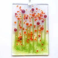 Quirky handmade red glass flower suncatcher with red and orange tactile beads and strings. Hole drilled at the top with white ribbon threaded through.
