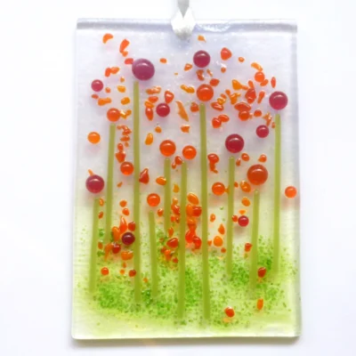 Quirky handmade red glass flower suncatcher with red and orange tactile beads and strings. Hole drilled at the top with white ribbon threaded through.