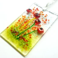 Red glass flower suncatcher at an angle hanging from a white ribbon.