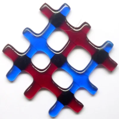 Small red and blue lattice fused glass suncatcher hanging from a clear wire. Glass strips of three red and three blue, have fused into a lattice design and has four holes in the middle.