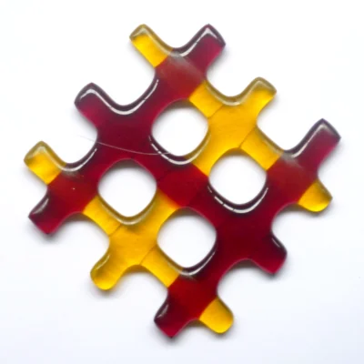 Small red and yellow lattice fused glass suncatcher. Three red and three yellow strips of glass have been fused in a lattice design. Hangs from a clear cord.