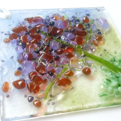 Close up of spring colours fused glass suncatcher, in the design of a tree, with colours of plum, lilac and green.