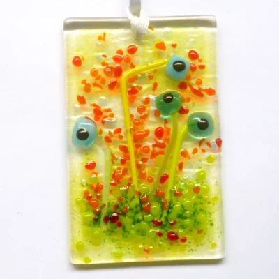 Rectangle turquoise glass flower suncatcher hanging from a white ribbon. Quirky square flowers with black centres, and red and green frit for decoration.