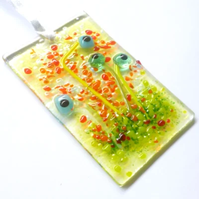 Rectangle turquoise glass flower suncatcher laying at an angle. Quirky square glass flowers with frit detail. Hangs from a white ribbon.