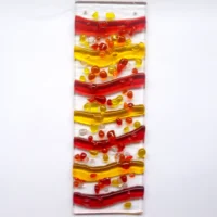 Colourful red, yellow and orange fused glass wave suncatcher at an angle hanging outside. Glass cut into wave shapes fused onto a clear glass, with large frit as decoration. Hangs from a clear cord.