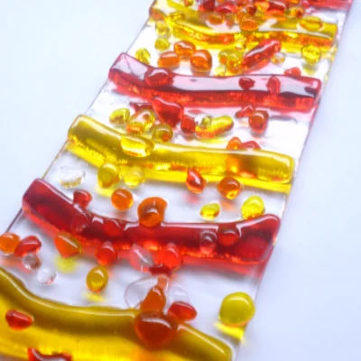 Close up of red, yellow and orange wave fused glass suncatcher, showing depth of glass.