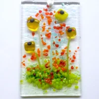 Rectangle yellow glass flower suncatcher with red, orange and green frit decoration. Square and tactile yellow glass represents flowers with green stringer stems. Hanging from a white ribbon.