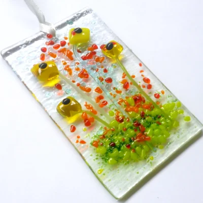 Unique yellow glass flower suncatcher laying at an angle. This tactile design hangs from a white ribbon.