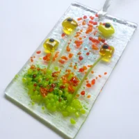 Laying at a slight angle this yellow fused glass flower suncatcher hangs from a white ribbon.